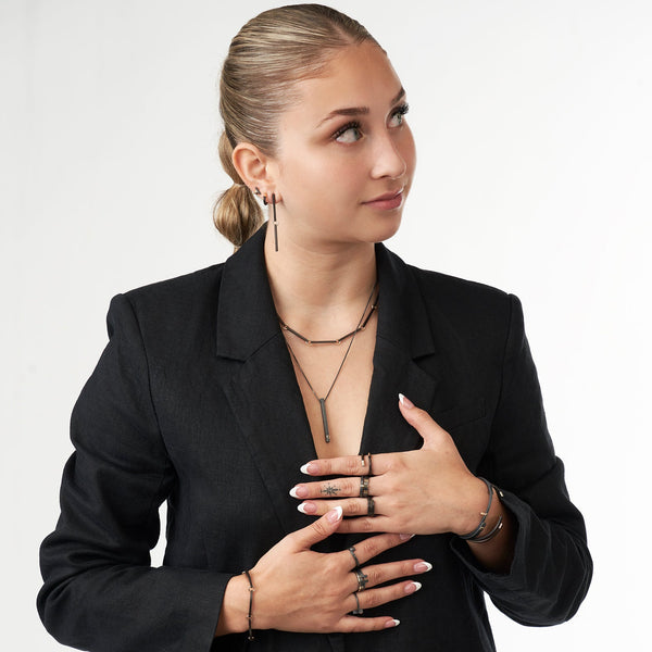 Model wearing a black blazer and the oxidized silver and 14k gold bracelet shown in the first image, styled with several other matching jewelry pieces in the same dark-and-gold color palette.